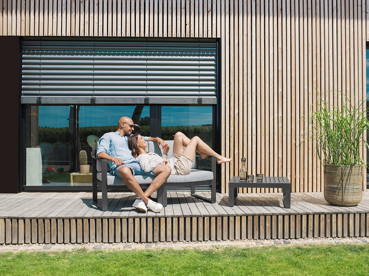 Frau und Mann liegen im Garten auf ein Sofa vor einem Holzhaus